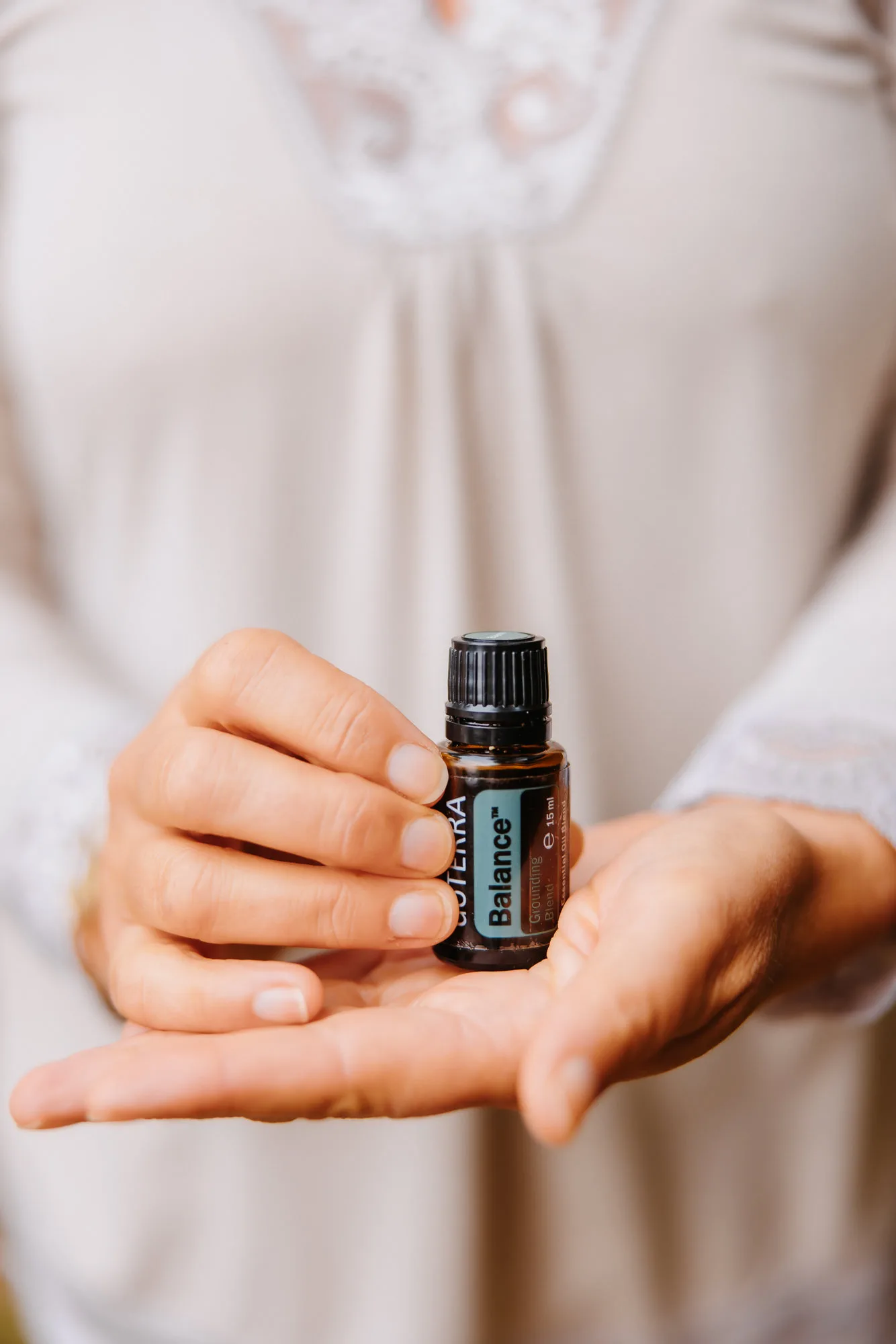 Primer plano de unas manos femeninas sosteniendo el aceite esencial Balance de dōTERRA.