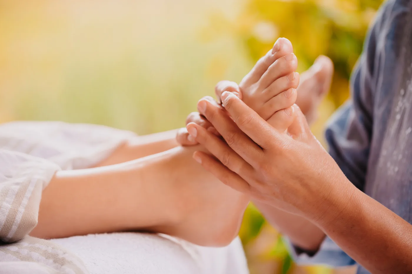 Weibliche Hände bei einer Fußreflexzonenmassage an den entspannt auf der Behandlungsliege ruhenden Füßen