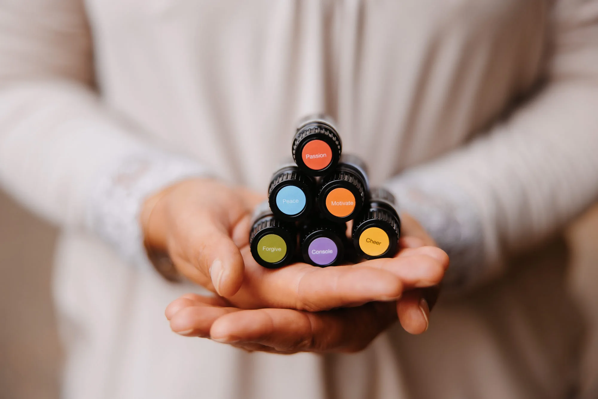Primer plano de unas manos femeninas sosteniendo los aceites esenciales de la colección Emotional Aromatherapy de dōTERRA, dispuestos en forma de pirámide